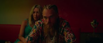 Movie still from “The Enforcer” (2022), directed by Richard Hughes – A man with a long beard is sitting next to a woman; Medium shot, Over the shoulder angle