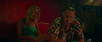 Movie still from “The Enforcer” (2022), directed by Richard Hughes – A man and a woman sitting next to each other on a couch; Medium shot, Low angle