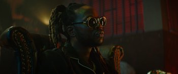Movie still from “The Enforcer” (2022), directed by Richard Hughes – A man with dreads and sunglasses is looking up; Close Up shot, Low angle
