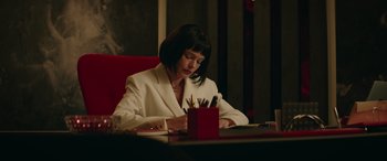 Movie still from “The Enforcer” (2022), directed by Richard Hughes – A woman sitting at a table writing on a piece of paper; Medium shot, Low angle