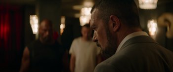 Movie still from “The Enforcer” (2022), directed by Richard Hughes – A person wearing a suit and tie; Close Up shot, Over the shoulder angle