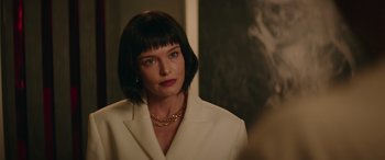 Movie still from “The Enforcer” (2022), directed by Richard Hughes – A woman in a white suit with a gold chain around her neck; Close Up shot, Over the shoulder angle