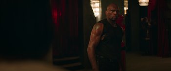 Movie still from “The Enforcer” (2022), directed by Richard Hughes – A man standing in a dark room with his arms crossed; Medium shot, Low angle