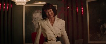 Movie still from “The Enforcer” (2022), directed by Richard Hughes – A woman wearing a white suit and a gold belt; Medium shot, High angle