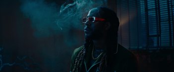 Movie still from “The Enforcer” (2022), directed by Richard Hughes – A man with dreadlocks smoking a cigarette in front of a brick wall; Close Up shot, Low angle