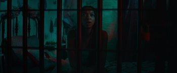 Movie still from “The Enforcer” (2022), directed by Richard Hughes – A woman sitting behind bars in a dark room; Close Up shot, Low angle