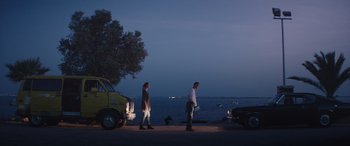 Movie still from “The Enforcer” (2022), directed by Richard Hughes – Two men walking on the side of the road near the water; Wide shot, Low angle