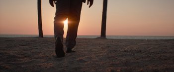 Movie still from “The Enforcer” (2022), directed by Richard Hughes – A person walking on the beach at sunset; Wide shot, Low angle