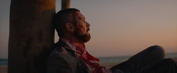 Movie still from “The Enforcer” (2022), directed by Richard Hughes – A man with a beard and a bloody bandage on his face; Medium shot, Low angle