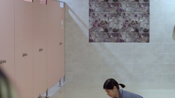 Movie still from “The Entitled” (2022), directed by Theodore Boborol – A woman is standing in a bathroom next to a pink stall; Wide shot, High angle