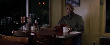 Movie still from “The Equalizer” (2014), directed by Antoine Fuqua – A man sitting at a table with a cup of coffee; Medium shot, Over the shoulder angle