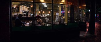 Movie still from “The Equalizer” (2014), directed by Antoine Fuqua – A woman sitting at a table in front of a restaurant; Extreme Wide shot, Over the shoulder angle