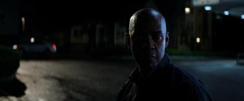 Movie still from “The Equalizer” (2014), directed by Antoine Fuqua – A man in a black shirt is standing in the dark; Close Up shot, Over the shoulder angle