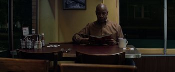 Movie still from “The Equalizer” (2014), directed by Antoine Fuqua – A man sitting at a table reading a book; Medium shot, Low angle
