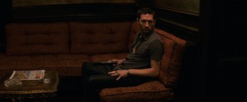 Movie still from “The Equalizer” (2014), directed by Antoine Fuqua – A man sitting on top of a red couch; Medium shot, High angle