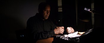Movie still from “The Equalizer” (2014), directed by Antoine Fuqua – A man sitting at a table looking at something in his hand; Medium shot, Low angle