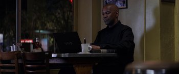 Movie still from “The Equalizer” (2014), directed by Antoine Fuqua – A man sitting in front of a laptop computer at a table; Medium shot, Low angle