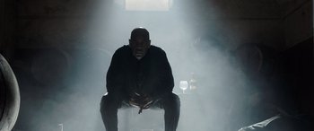 Movie still from “The Equalizer 3” (2023), directed by Antoine Fuqua – A man sitting on a chair in a room with smoke coming out of the ceiling; Medium shot, Low angle
