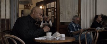 Movie still from “The Equalizer 3” (2023), directed by Antoine Fuqua – A man sitting at a table with a cup of coffee; Medium shot, Low angle