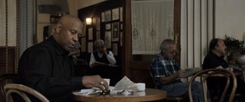Movie still from “The Equalizer 3” (2023), directed by Antoine Fuqua – A man sitting at a table in front of two other men; Medium shot, Low angle