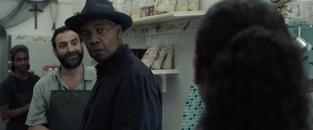 Movie still from “The Equalizer 3” (2023), directed by Antoine Fuqua – A man wearing a black hat and a black shirt; Close Up shot, Over the shoulder angle