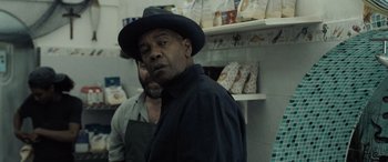 Movie still from “The Equalizer 3” (2023), directed by Antoine Fuqua – A man wearing a hat standing next to another man in a kitchen; Medium shot, Over the shoulder angle
