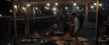 Movie still from “The Equalizer 3” (2023), directed by Antoine Fuqua – A group of people standing around a table with plates of food on top of it; Wide shot, High angle