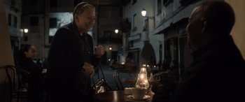 Movie still from “The Equalizer 3” (2023), directed by Antoine Fuqua – An older woman sitting at a table with a lit candle; Medium shot, Over the shoulder angle
