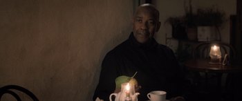 Movie still from “The Equalizer 3” (2023), directed by Antoine Fuqua – A man sitting in front of a tea pot with a lit candle; Medium shot, Low angle