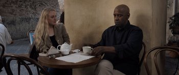 Movie still from “The Equalizer 3” (2023), directed by Antoine Fuqua – A man and a woman sitting at a table with a cup of tea; Medium shot, Over the shoulder angle
