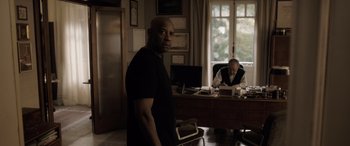 Movie still from “The Equalizer 3” (2023), directed by Antoine Fuqua – A man standing in front of a desk in a room; Medium shot, Over the shoulder angle