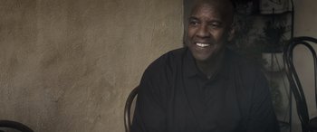 Movie still from “The Equalizer 3” (2023), directed by Antoine Fuqua – A man sitting in a chair smiling for the camera; Close Up shot, Low angle