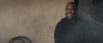 Movie still from “The Equalizer 3” (2023), directed by Antoine Fuqua – A man smiling for the camera in front of a wall; Medium shot, Low angle