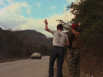 Movie still from “The Evil Dead” (1981), directed by Sam Raimi – Two men standing next to each other on the side of the road; Wide shot, Over the shoulder angle