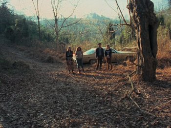 Movie still from “The Evil Dead” (1981), directed by Sam Raimi – A group of people standing next to an old car; Wide shot, High angle