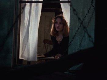 Movie still from “The Evil Dead” (1981), directed by Sam Raimi – A woman sitting at a table in front of a window; Medium shot, Low angle