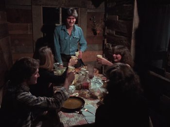 Movie still from “The Evil Dead” (1981), directed by Sam Raimi – A group of people sitting around a table eating food; Medium shot, High angle