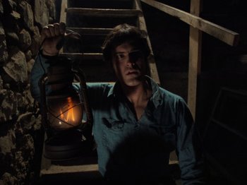 Movie still from “The Evil Dead” (1981), directed by Sam Raimi – A man holding a lantern while standing on some stairs; Medium shot, High angle