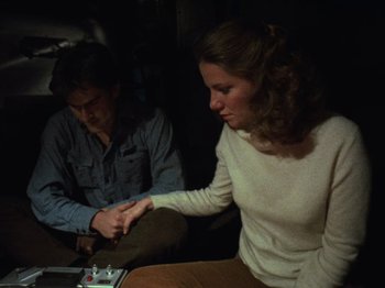 Movie still from “The Evil Dead” (1981), directed by Sam Raimi – A man and a woman sitting in a dark room; Medium shot, High angle