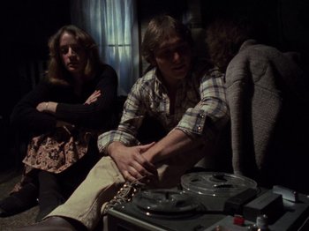 Movie still from “The Evil Dead” (1981), directed by Sam Raimi – A man sitting on top of a couch next to a woman; Medium shot, High angle