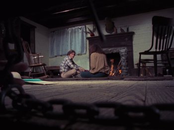 Movie still from “The Evil Dead” (1981), directed by Sam Raimi – A man and a woman sitting in front of a fireplace; Wide shot, High angle