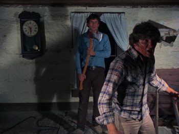 Movie still from “The Evil Dead” (1981), directed by Sam Raimi – A man holding an axe in front of another man in front of a clock; Medium shot, Low angle
