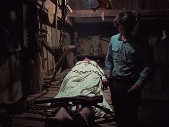 Movie still from “The Evil Dead” (1981), directed by Sam Raimi – A man standing next to a body in chains; Wide shot, Low angle