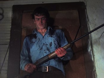 Movie still from “The Evil Dead” (1981), directed by Sam Raimi – A man holding a rifle while wearing a blue shirt; Medium shot, Low angle