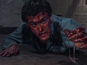 Movie still from “The Evil Dead” (1981), directed by Sam Raimi – A man with blood all over his face is laying on the ground; Close Up shot, Overhead angle