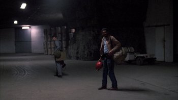 Movie still from “Day of the Dead” (1985), directed by George A. Romero – A man holding a fire hydrant in a dark room; Wide shot, High angle