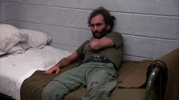 Movie still from “Day of the Dead” (1985), directed by George A. Romero – A man sitting on a bed with his arms crossed; Medium shot, High angle
