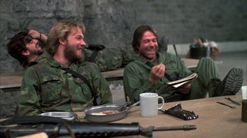 Movie still from “Day of the Dead” (1985), directed by George A. Romero – A couple of men sitting next to each other at a table; Medium shot, Over the shoulder angle