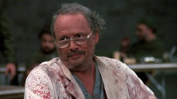 Movie still from “Day of the Dead” (1985), directed by George A. Romero – An older man with a beard and glasses is looking at the camera; Close Up shot, Low angle
