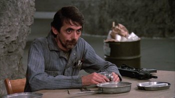 Movie still from “Day of the Dead” (1985), directed by George A. Romero – A man sitting at a table in front of a pan; Close Up shot, High angle